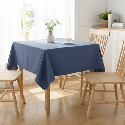 Airforce blue square tablecloth on a small square kitchen table with simple wooden dining chairs in a bright cosy UK home setting with flowers and tea